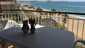 Een balkon met een tafel, stoelen en uitzicht op het strand en de zee.