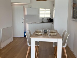 A dining area with a table set for four, white chairs, a kitchen in the background, and a door leading to another room. - Apartment with sea view - 3 guests (San Antonio de Calonge)