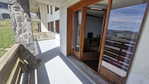 Ein Balkon mit Steinmauern, einem Holzgeländer und Blick auf ein Gebäude mit Fenstern und einer Tür.