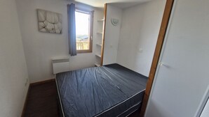 Ein kleines Zimmer mit einem Einzelbett, einem Fenster, einer Heizung und einem an der Wand befestigten Regal.