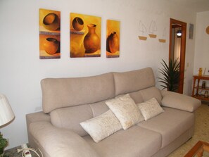 Ein beiges Sofa mit gemusterten Kissen, einer Lampe und Wandbildern mit Keramikdarstellungen.