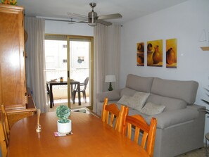 Ein Wohnzimmer mit einem Holzesstisch, einem beigefarbenen Sofa, einem Deckenventilator und drei Bildern an der Wand.