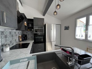 Una cocina moderna con un refrigerador, horno y microondas de acero inoxidable. Hay un fregadero con un escurreplatos, y una ventana con cortinas.