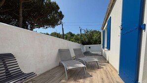 Een overdekt terras met een bank en twee stoelen, een blauwe deur en een witte muur.