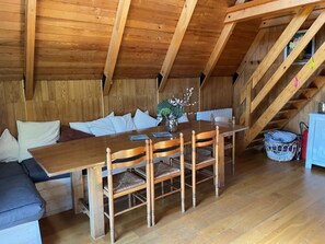 Ein Holzesstisch mit Stühlen, eine Couch und eine Treppe in einem Zimmer mit Holzwänden und einer geneigten Decke.