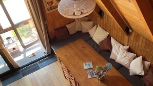 Ett matbord i trä med stolar, en flätad taklampa och en soffa med kuddar.