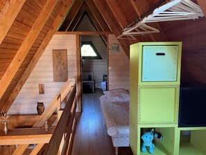 Ein Schlafzimmer im Landhausstil mit Schlafgalerie, geneigter Decke, einem Bett, einem kleinen Tisch mit einer Vase und einem grünen Schrank mit Fernseher.