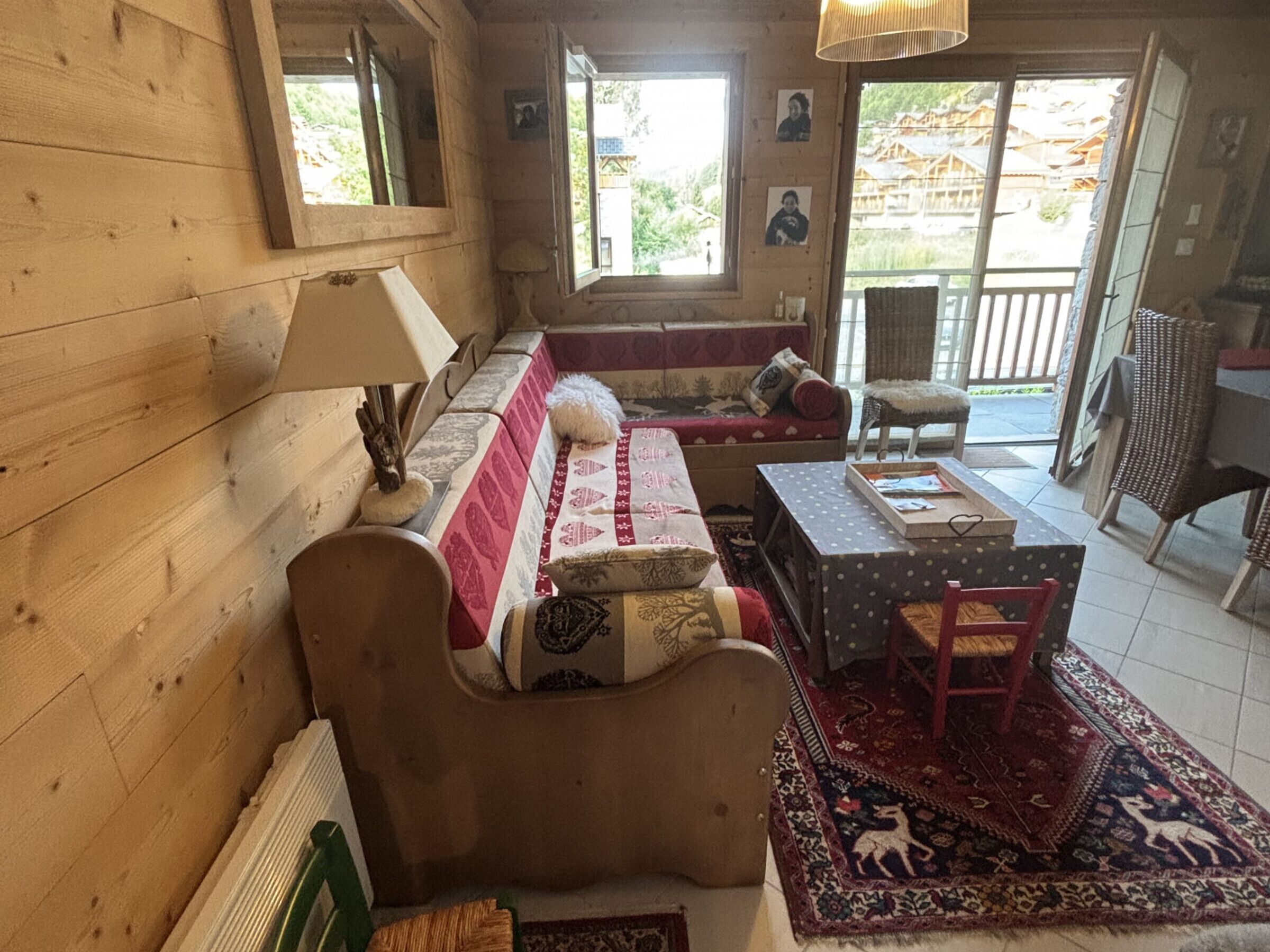A wooden interior with a sofa, a table, and a chair. There are windows and a view of the outside.
