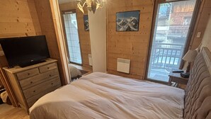 A bedroom with a bed, a dresser, a television, a radiator, and a window with a view. - Comfortable apartment for 8 guests with private garage (Les Gets)