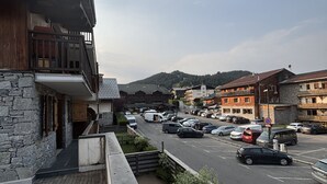 A street view with parked cars, a building with a stone facade, and a mountainous backdrop. - Comfortable apartment for 8 guests with private garage (Les Gets)