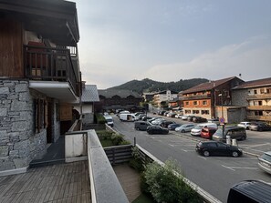Straßenansicht mit parkenden Autos, einem Gebäude mit steinverkleideter Fassade und einer Bergkulisse im Hintergrund.