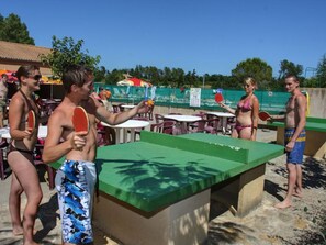 Un espace aménagé au bord de la piscine, comprenant une table de ping-pong, des sièges d’extérieur et une piscine.