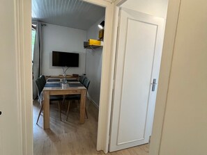 Ein Essbereich mit Tisch, Stühlen, einem Flachbildfernseher und einem Regal mit Gegenständen.