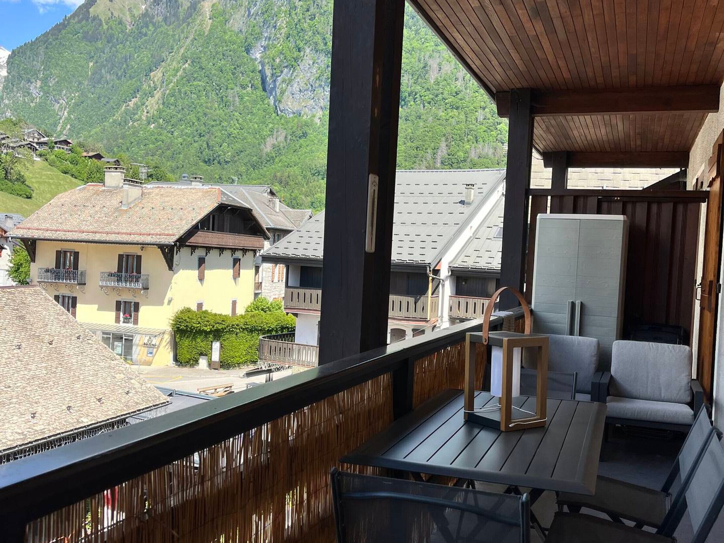 Un balcón con vistas a casas de montaña, techo de madera y una mesa con sillas.