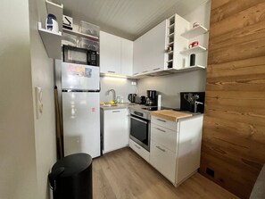 Eine kleine Küche mit weißen Schränken, einer Mikrowelle, einer Kaffeemaschine und einem Spülbecken.