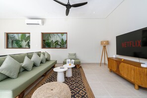 Ein modernes Wohnzimmer mit einer Couch, zwei Beistelltischen, einem Couchtisch, einem Fernseher und einem Deckenventilator.