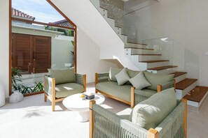 En moderne stue med en sofasæt, et sofabord og en trappe med glasgelændere.