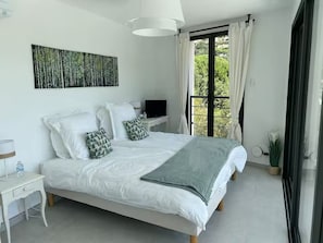 Ein modernes Schlafzimmer mit einem großen Bett, einem Flachbildfernseher, einem Nachttisch mit Lampe und einem Fenster mit Vorhängen.