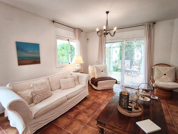 A living room with a sofa, a coffee table with decorative items, a lamp, and a view through a glass door. - Villa Cava, Calonge - Costa Brava (Calonge i Sant Antoni)