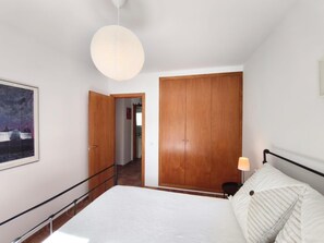A bedroom with a bed, a wooden wardrobe, a door leading to another room, and a hanging light fixture. - Villa Cava, Calonge - Costa Brava (Calonge i Sant Antoni)