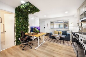 Ein moderner Wohnraum mit einer grünen Wand, einer Couch, einem Schreibtisch mit Computer und einer Waschmaschine.