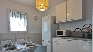 A compact kitchen with a dining table set for two, a microwave, a refrigerator, and a sink with a dish rack. - Studio cabin, parking, near beach - 4 guests (Le Grau-du-Roi)