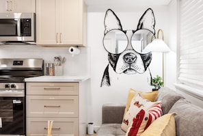 Eine Küche mit modernen Geräten, einem Wandbild von einem Hund und einem grauen Sofa mit gemusterten Kissen.