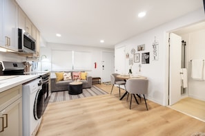 Eine moderne Küche mit eingebauten Geräten, ein Essbereich mit rundem Tisch und Stühlen sowie ein Wohnzimmer mit Sofa und Couchtisch.