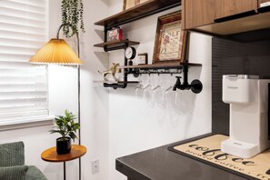 A kitchen with a coffee machine, a shelf with a framed certificate, a hanging plant, and a small table with a potted plant. - Modern Industrial Seattle Suite | Workspace + Kitchen (Seattle)
