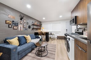 A modern kitchen with a washing machine, a dining table with chairs, a sofa, and wall decorations. - Modern Industrial Seattle Suite | Workspace + Kitchen (Seattle)
