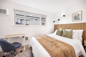 A bedroom with a bed, desk, chair, window, and artwork. - Modern Industrial Seattle Suite | Workspace + Kitchen (Seattle)