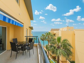 Ein Balkon mit Tisch und Stühlen, Blick aufs Meer, und ein Gebäude mit gelben Wänden.