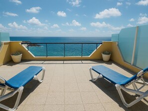 Ein Balkon mit zwei Liegestühlen, Pflanzen in Töpfen und Blick aufs Meer.