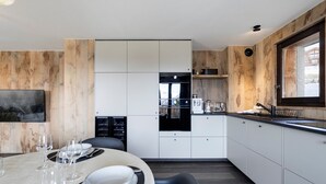 Eine moderne Küche mit integrierten Geräten, ein Essbereich mit rundem Tisch und ein großes Fenster.