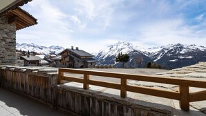 Eine hölzerne Bank mit Blick auf eine Berglandschaft, deren Gipfel mit Schnee bedeckt sind, unter einem klaren Himmel.