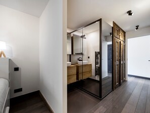 Ein modernes Badezimmer mit großem Spiegel, Holzkosmetikschrank und Glasabtrennung.