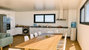 Uma cozinha moderna com máquina de lavar embutida, um espaço de refeições com mesa de madeira e cadeiras brancas, e uma janela grande que oferece vista para o exterior.