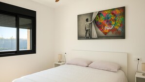 Quarto com cama, janela, quadro pendurado na parede e mesas de cabeceira.