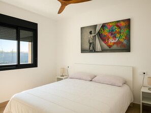 Ein Schlafzimmer mit Bett, Fenster, einem Wandbild und Nachttischen.