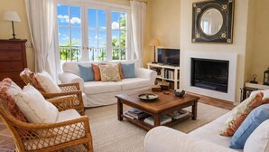 Ein Wohnzimmer mit einer Couch, zwei Korbstühlen, einem Couchtisch, einem Kamin, einem Fernseher und einem Bücherregal.