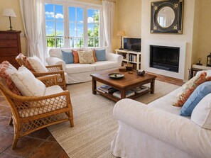 Ein Wohnzimmer mit einer Couch, zwei Korbstühlen, einem Couchtisch, einem Kamin, einem Fernseher und einem Bücherregal.