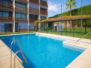 A swimming pool with metal railings, a tiled deck, and a building with striped awnings in the background. - Renovated Apartment in Marbella with Pool (Marbella)