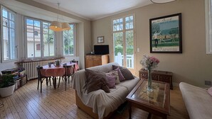 Une pièce chaleureuse avec un plancher en bois, un canapé, une table à manger avec des chaises, un téléviseur et un tableau accroché au mur.