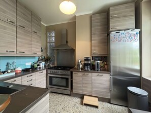 A modern kitchen with wooden cabinets, a stainless steel stove, a refrigerator, and a coffee maker.