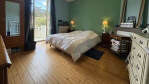 Une chambre à coucher avec un lit, une commode, un miroir, une fenêtre avec des rideaux et une porte.