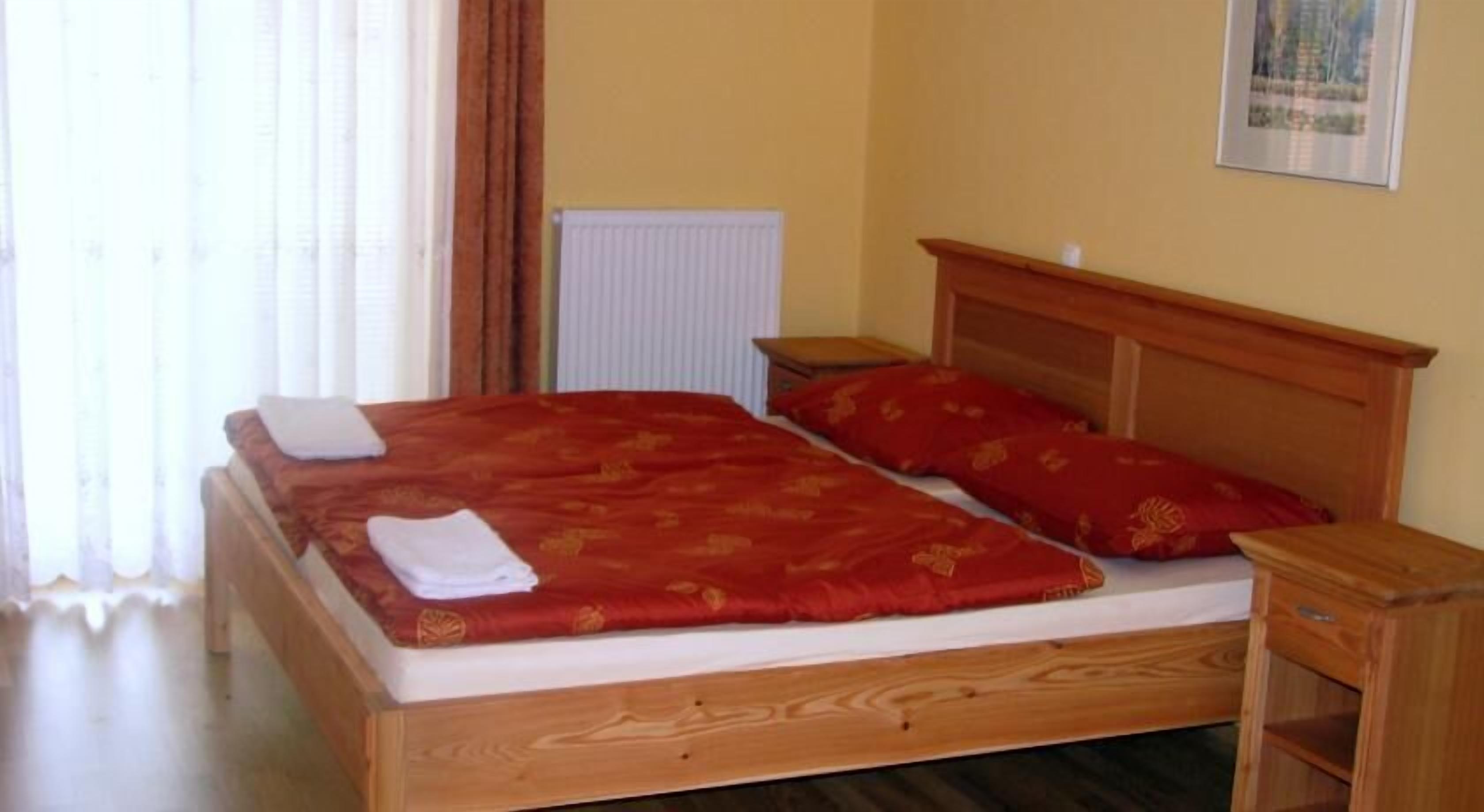 Uma cama de solteiro com cabeceira de madeira, colcha vermelha e duas almofadas.