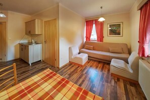 A compact living space with a kitchenette, a sofa, a dining table, and a checkered rug. - Garni Hotel Rute (Kranjska Gora)