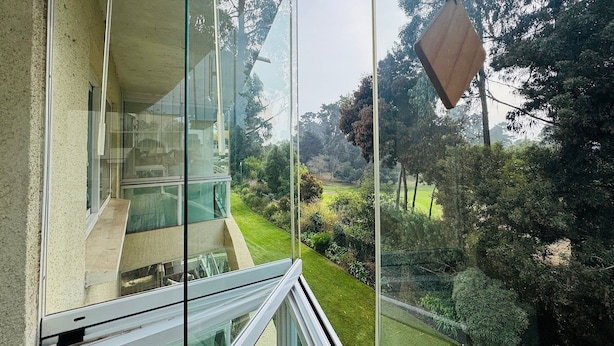 A modern building with large glass windows, a view of a green landscape, and a hanging wooden object.