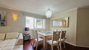 A dining area with a table and chairs, a chandelier, a couch, and a painting on the wall.