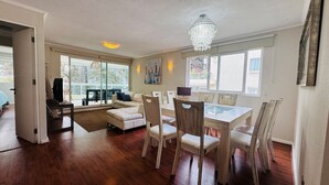 A spacious living area with a dining table, chairs, a sofa, and a chandelier.